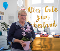 Regina Bauerschäfer steht mit einem Blumenpräsent in ihrem geschmückten Büro